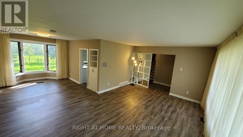 A spacious room with wooden flooring and a large window with curtains.