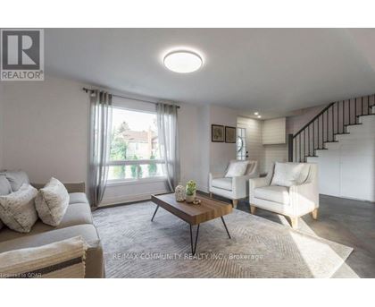 A well-lit living room with a grey sofa, a wooden coffee table, and a staircase with a black railing.