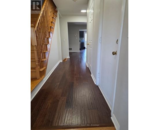 A hallway with wood flooring and a staircase on the left.