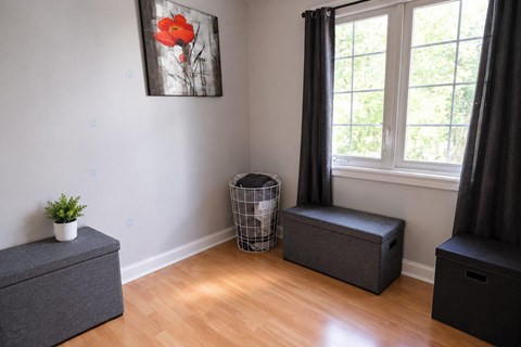 A room with a grey ottoman, a black ottoman, and a painting of a red flower on the wall.