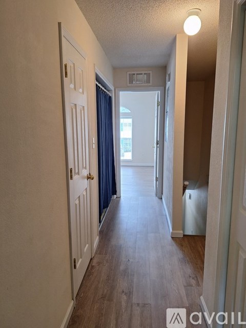 A long hallway with a door on the left and a window with blue curtains on the right.