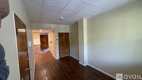 A room with wooden floors and white walls, with a door on the left and another door in the distance.