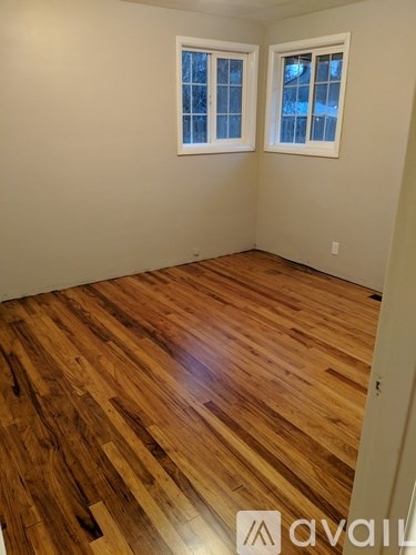 A room with wooden flooring and two windows.