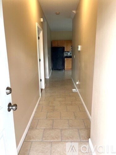 A hallway with a door on the left and a kitchen in the distance.