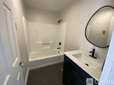 A bathroom with a white sink, a round mirror, and a white bathtub.