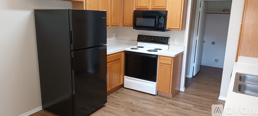 A black refrigerator is in a kitchen with wooden cabinets and a black microwave.