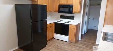 A black refrigerator is in a kitchen with wooden cabinets and a black microwave.