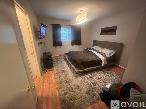 A bedroom with a bed, a rug, a TV, and a window with black curtains.