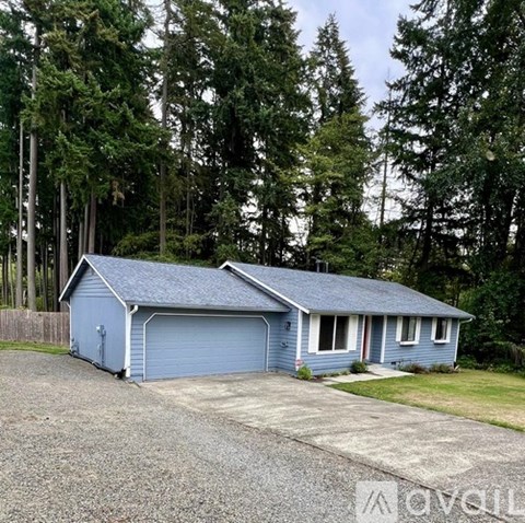 A blue house with a grey roof is surrounded by trees.