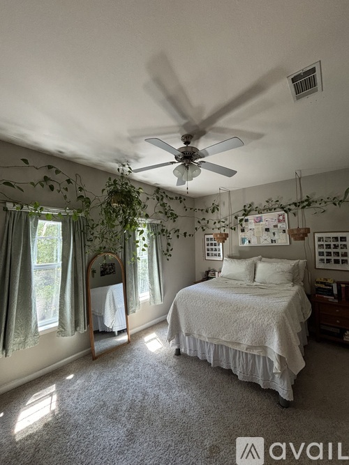 A bedroom with a bed, a fan, and a window with curtains.