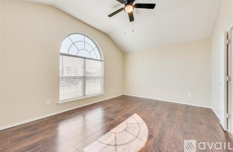 A room with a fan, window, and wooden floor.