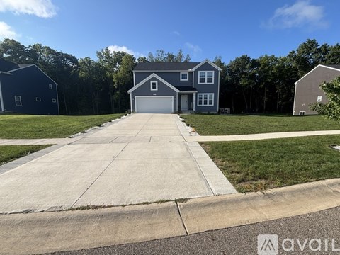 A house with a grey roof and a white garage door is surrounded by a green lawn.