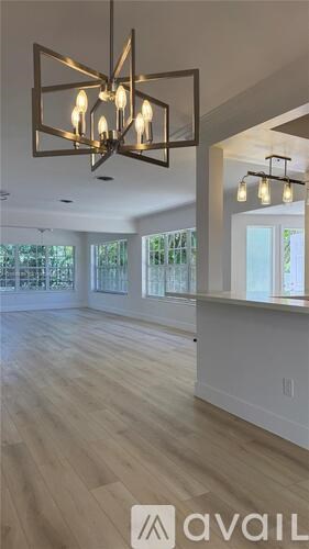 A modern chandelier hangs over a spacious room with wood flooring and large windows.