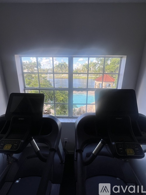 Two treadmills are in front of a window with a view of a pool and a building.