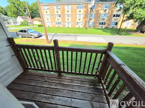 A wooden deck with a view of a grassy area and a building in the background.
