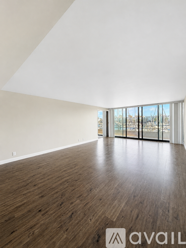 A spacious room with wooden flooring and large windows.
