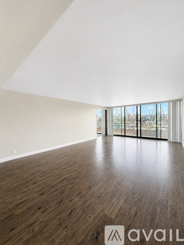 A spacious room with wooden flooring and large windows.