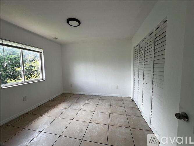 A room with white walls, a tiled floor, and a window with a view of trees.