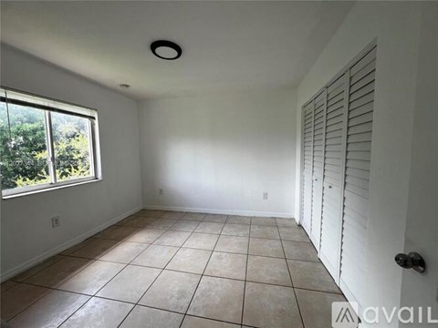 A room with white walls, a tiled floor, and a window with a view of trees.