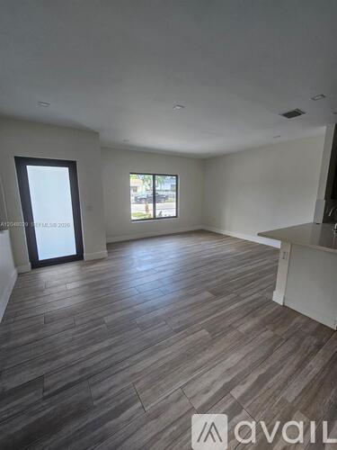 A spacious room with wooden flooring and a large window.