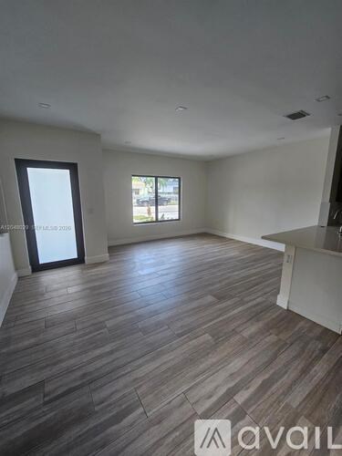 A spacious room with wooden flooring and a large window.