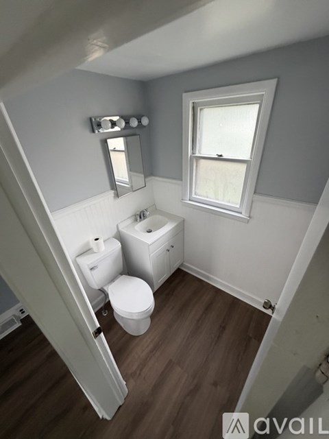 A bathroom with a toilet, sink, mirror and window.