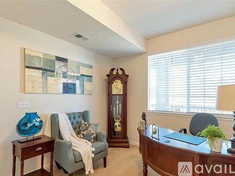A living room with a grey couch, a wooden table, a lamp, a vase, a clock, and a painting on the wall.