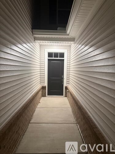 A black door is at the end of a hallway with white walls and a skylight.