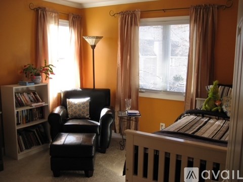 A living room with a black leather chair and ottoman, a bookshelf filled with books, and a bed with a striped comforter.