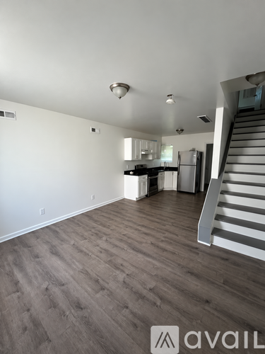 A spacious room with wooden flooring and a staircase on the right side.