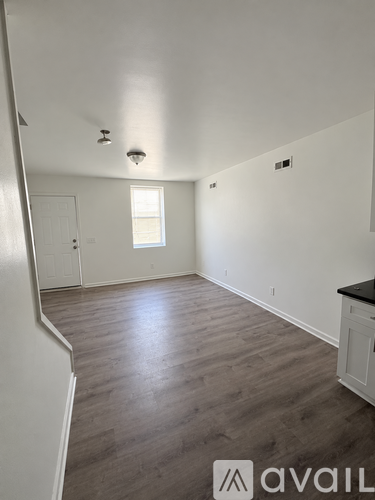 A room with wooden floors and white walls, with a window and a door visible.
