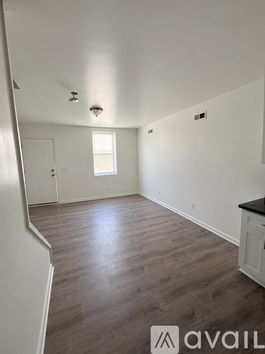 A room with wooden floors and white walls, with a window and a door visible.