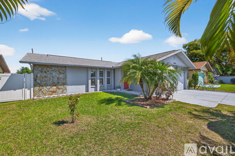 A house with a white exterior and a stone wall is surrounded by a well-manicured lawn.