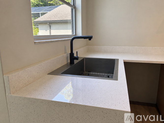 A kitchen sink with a black faucet and a window in the background.
