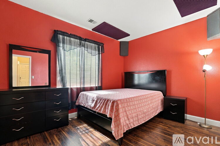 A bedroom with a bed, dresser, and a window with curtains.
