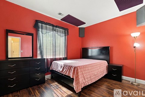 A bedroom with a bed, dresser, and a window with curtains.