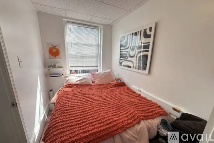 A bedroom with a bed covered in a red blanket and a painting on the wall.