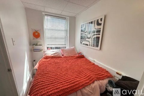 A bedroom with a bed covered in a red blanket and a painting on the wall.