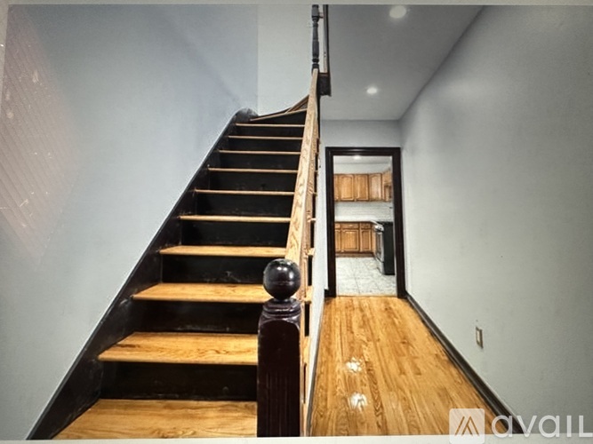 A wooden staircase with a black railing leads to a room with a tiled floor.