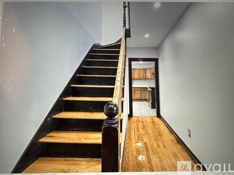 A wooden staircase with a black railing leads to a room with a tiled floor.