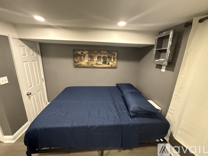 A bed with a blue cover is in a room with a white door and a picture on the wall.