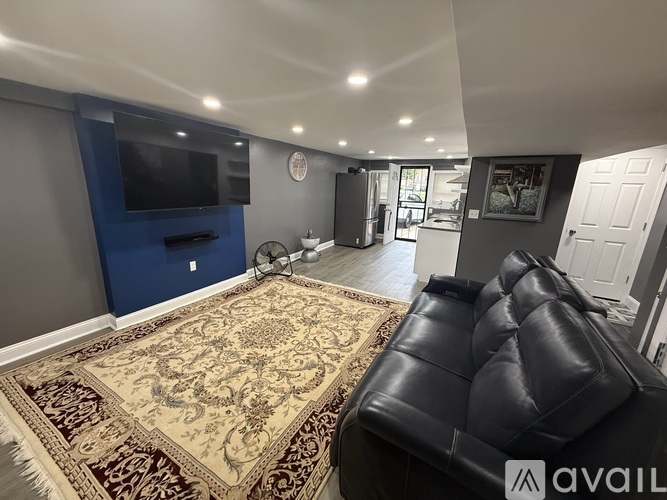 A living room with a black leather couch and a large rug.