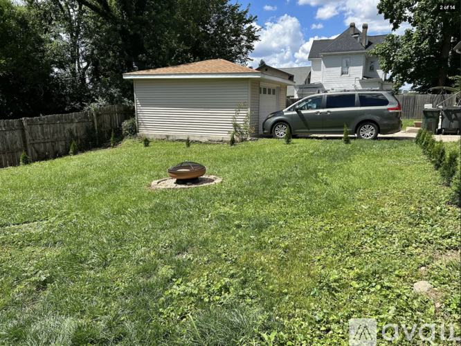 A backyard with a green lawn and a silver minivan parked in the driveway.