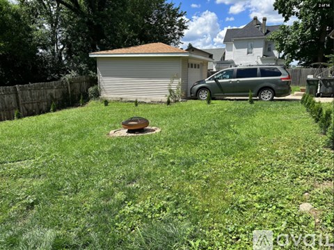A backyard with a green lawn and a silver minivan parked in the driveway.