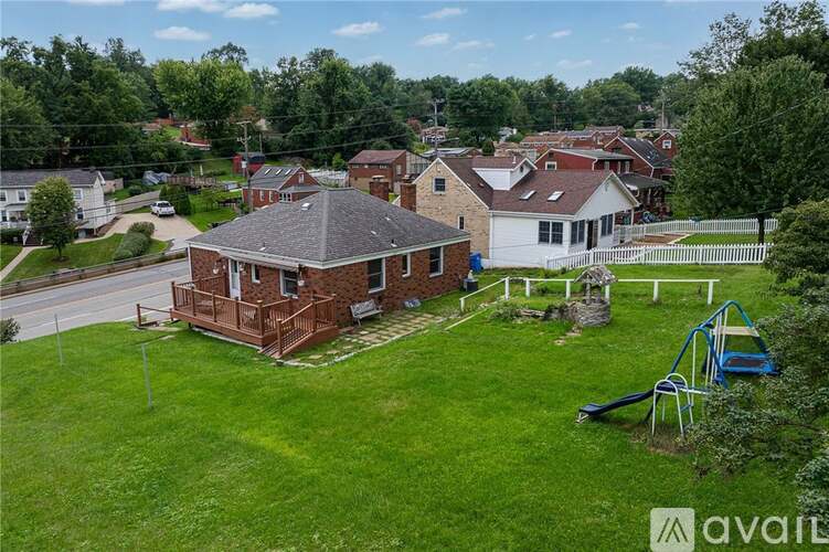 A house with a red brick exterior is surrounded by a white picket fence and has a green lawn.