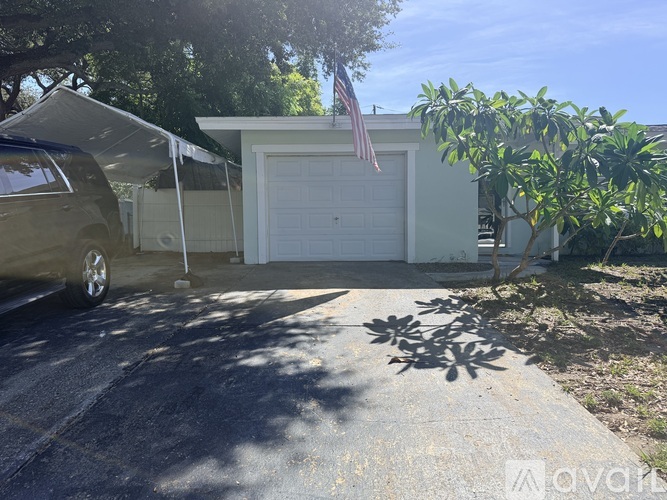 A car is parked in front of a house with a garage door and an American flag.