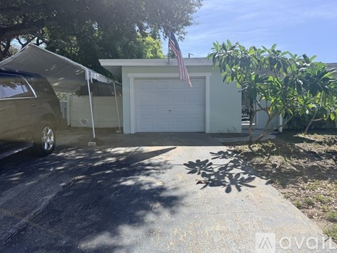 A car is parked in front of a house with a garage door and an American flag.