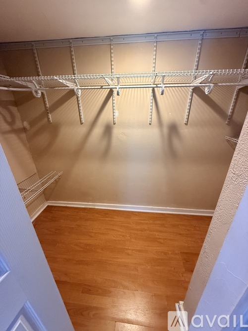 Empty walk-in closet with wooden floors and white shelving.