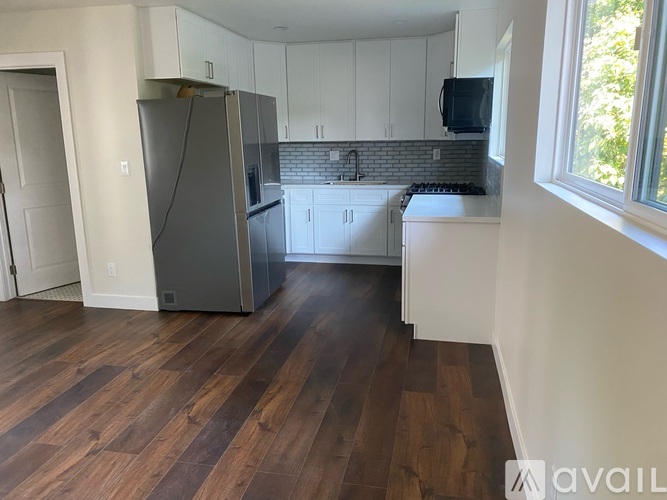 A kitchen with a refrigerator, cabinets, and a window.