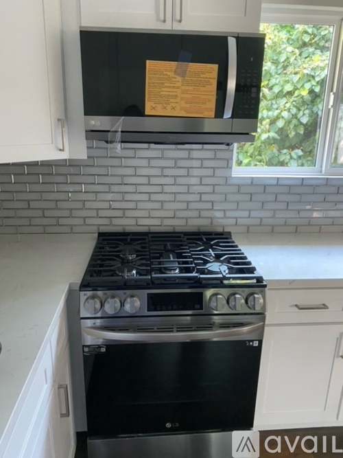 A black stove top oven with four burners and a note taped to the microwave above it.